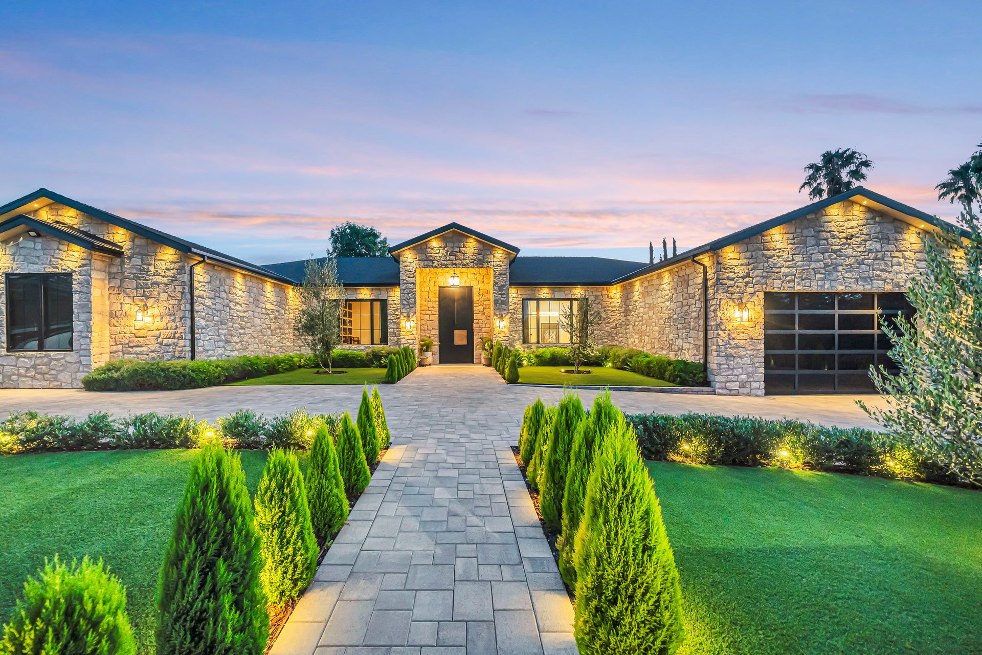 Custom home exterior lit at dusk with landscaped entry