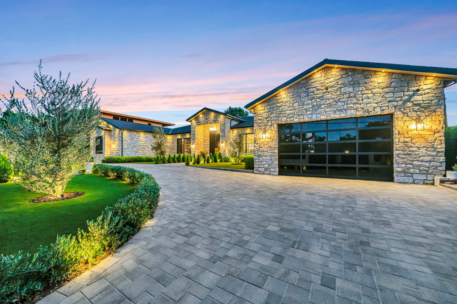 Paver driveway and stone home lit at dusk